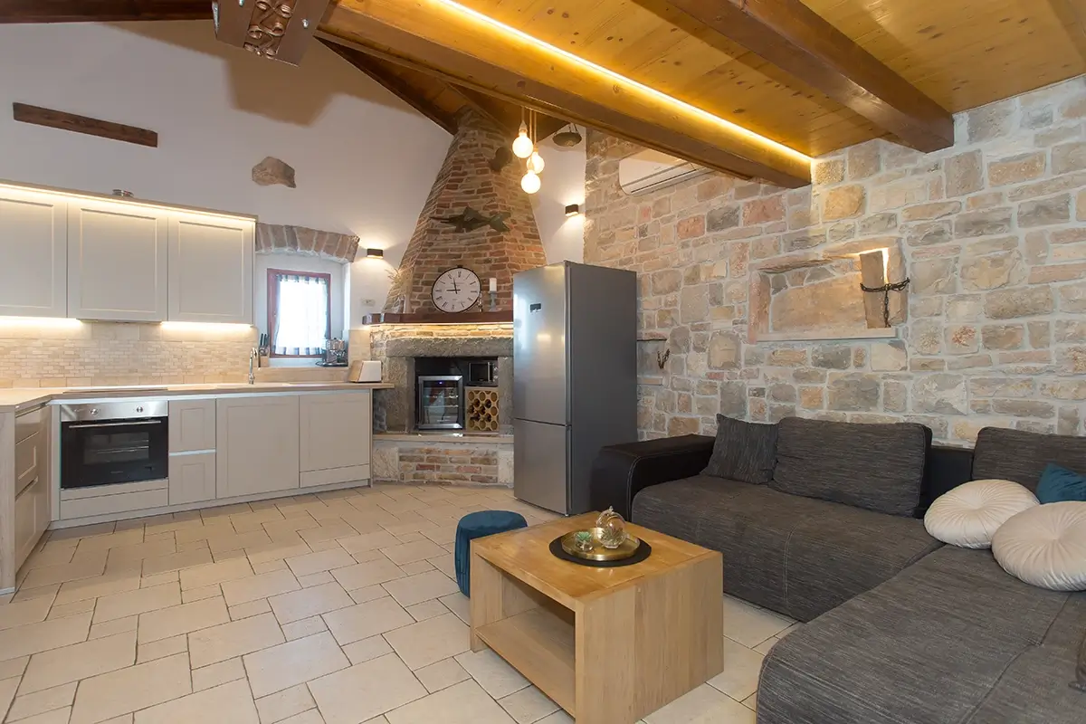 Image of a white kitchen with a stone wine rack, large sofa, stone walls, and a wooden ceiling.